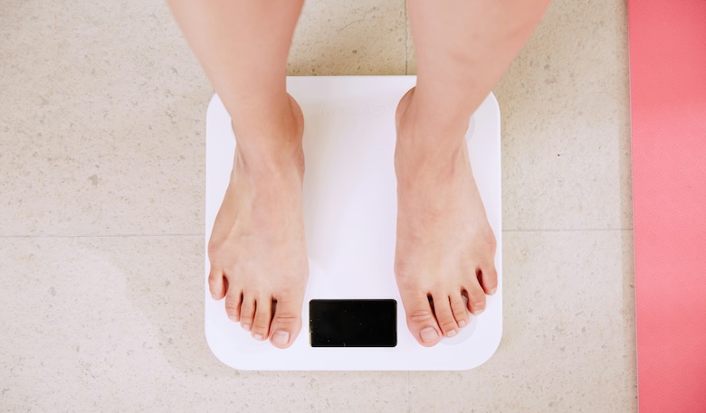 体重計に乗って体重を測っている女性の画像